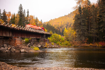 Wall Mural - Red fuel truck at wooden bridge over mountain river in autumn