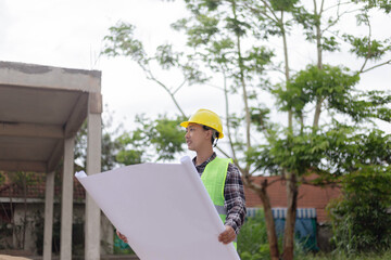engineer concept The constructing manipulator who wears a hard yellow hat, dark-toned plaid blouse and soft green vest looking at the processing building construction