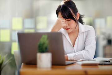 Tired frustrated asian businesswoman feeling stressed, upset executives sitting near laptop, holding head in hands, worried about business problem failure, depressed by bad news,