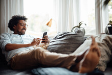 Happy Man Using Smart Phone Sitting On Sofa At Home