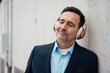 © Westend61 - Smiling businessman with eyes closed listening music through wireless headphones by wall