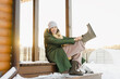 © Westend61 - Happy woman wearing boots sitting at porch of house in snowy garden