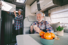 Senior Man Having Coffee With Woman Opening Cabinet In Background At Motor Home