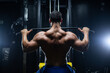 Handsome fitness man is performing back workouts using thrust of the upper block machine in a gym, back view