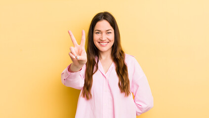 pretty caucasian woman smiling and looking happy, carefree and positive, gesturing victory or peace with one hand