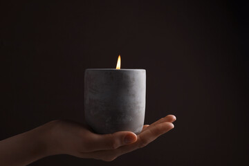 Poster - Woman with lit candle in concrete holder against dark brown background, closeup