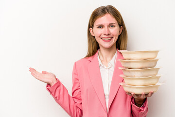 Young business English woman holding tupperware of food isolated on white background showing a copy space on a palm and holding another hand on waist.