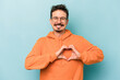 © Asier - Young caucasian man isolated on blue background smiling and showing a heart shape with hands.