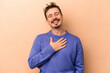 © Asier - Young caucasian man isolated on beige background laughs out loudly keeping hand on chest.