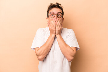 Wall Mural - Young caucasian man isolated on beige background shocked, covering mouth with hands, anxious to discover something new.