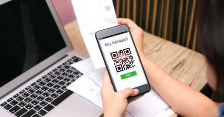 QR CODE scanning concept.Hands holding mobile phone on blurred utility bill on wooden table as backgrounds