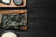 Dry nori sheets, rice, soy sauce and chopsticks on black wooden table, flat lay. Space for text