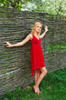 © Sergios - Young beautiful blonde in a red dress in a blooming garden against the background of a hedge of twigs. Spring outdoor