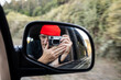 © Cavan Images - Person taking self portrait in rearview mirror of car while driving