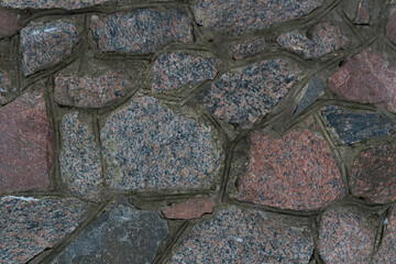 Wall Mural - Part of a textured stone wall, with a beautiful texture of wild stone. Part of the masonry walls of the old bastion. Wild stone bonded with cement mortar.