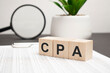 wooden cubes with letters CPA Certified Public Accountant on white table with keyboard and glasses