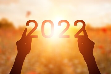 Wall Mural - 2022 is supported by hands on the background of a sunny sunset.