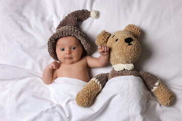 Canvas Print - Cute little baby with toy bear lying under blanket in bed, top view