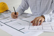 © New Africa - Architect working with construction drawings indoors, closeup