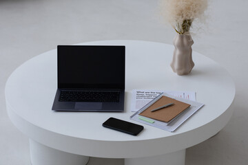 Wall Mural - Small minimal round table of white color with laptop, mobile phone, notebook, papers and vase with dry wildflowers