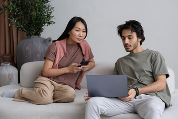 Poster - Two young interracial employees looking at laptop screen during presentation while sitting on sofa and working from home