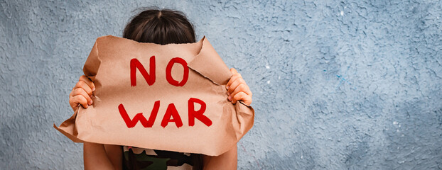 child raises a banner with the inscription no war, standing on the gray concrete background of the studio.