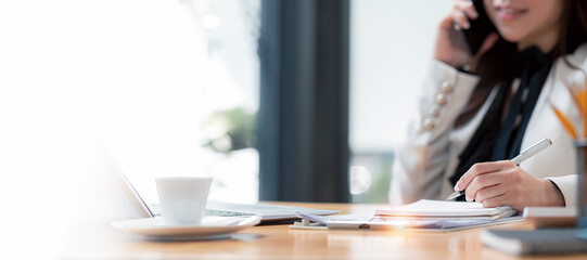 Wall Mural - young woman in suit using mobile phone, thinking and writing business plan on notebook at desk in modern office. room, copy space.