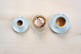 Three cups with various coffee, espresso, cappuccino and lungo crema on a light wooden table, copy space, high angle view from above