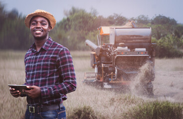 African Farmer holding tablet for combine harvester guidance and control on a background of combine harvester.Smart Farming Agriculture or Cultivation concept