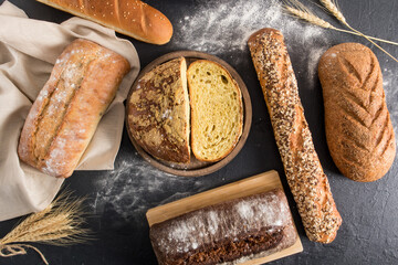 Wall Mural - an assortment of homemade freshly baked bread on a black background with flour and ears of corn. bread background. top view.