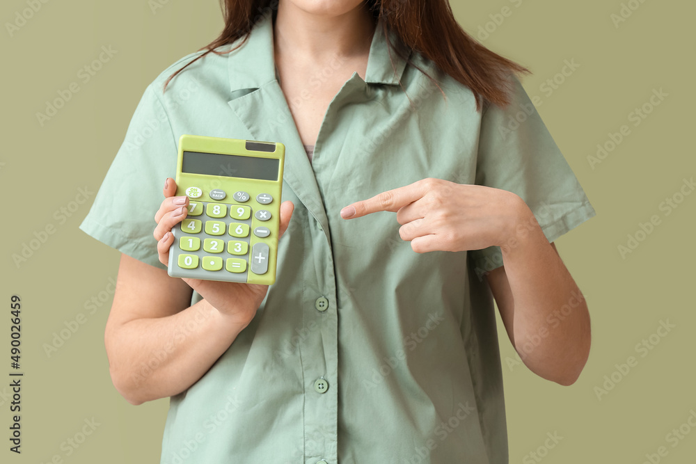 Young woman with calculator on green background