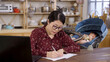 © PRPicturesProduction - asian lady pushing glasses while staring at the computer screen is reviewing report on the dining table and turning back to check and hold the bottle for her baby.