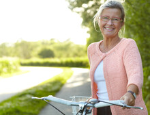 She Enjoys Healthy Outdoor Activities - Cycling. Smiling Senior Woman Standing On A Country Lane With Her Bicycle.