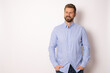 © Danko - Portrait of charming successful young man in blue shirt, smiling broadly with self-assured expression while holding hands in pockets over white background. Business concept.