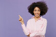 © ViDi Studio - Young fun woman of African American ethnicity 20s in pink striped shirt point index finger aside on workspace area mock up copy space isolated on plain pastel light purple background studio portrait