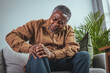 © Dragana Gordic - Photo of mature, elderly man sitting on a sofa in the living room at home and touching his knee by the pain during the day. Mature man massaging his painful knee.