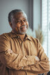 © Dragana Gordic - Side view of a happy African retired elderly man standing at home by the window. A satisfied old man looks out the window and smiles as he stands by the window