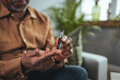 © Dragana Gordic - A modern African man sits at a table in the living room and takes blood from his finger due to diabetes.