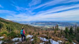 Fototapeta Na drzwi - Woman with backpack and a scenic view on the Drava river in the Rosental valley on the way to Sinacher Gupf in Carinthia, Austria. Forest in early spring. Austrian Alps mountain ranges on sunny day