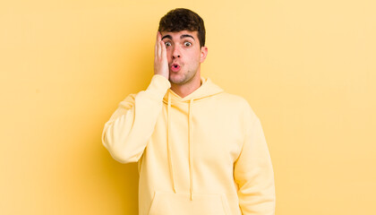 Wall Mural - young handsome man feeling shocked and astonished holding face to hand in disbelief with mouth wide open