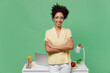 © ViDi Studio - Young employee business woman of African American ethnicity in shirt stand work at white office desk pc laptop hold hands crossed folded isolated on plain green background. Achievement career concept.