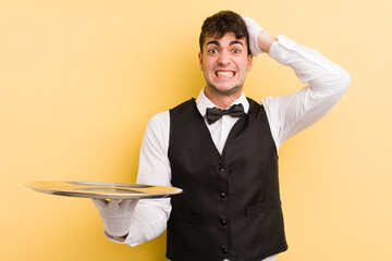 Wall Mural - young handsome man feeling stressed, anxious or scared, with hands on head. waiter and tray concept