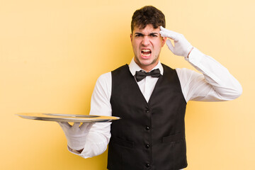 Wall Mural - young handsome man feeling confused and puzzled, showing you are insane. waiter and tray concept