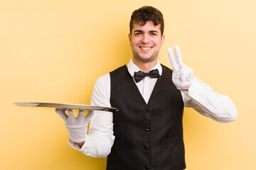 Wall Mural - young handsome man smiling and looking friendly, showing number two. waiter and tray concept