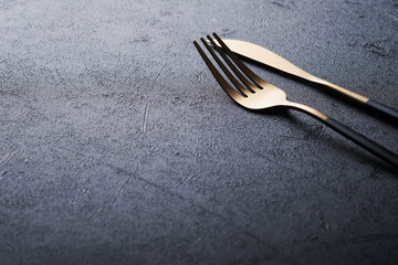 Wall Mural - Gold spoon, fork, knife and clean empty black plate. Set of stylish black and gold cutlery on black background. Fashionable and luxury eating. Top view. Copy space for your text.