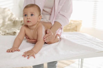 Mother applying body cream on her little baby at home, closeup