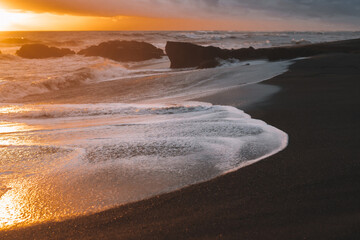 Golden ocean waves crash and foam on the black sand beach during sunset time in Canggu, Bali