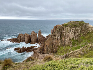 Poster - Scenic view of rocky cliffs surrounded by the ocean on cloudy sky backgroun