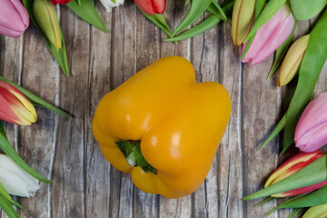 Canvas Print - Top view of yellow bell pepper with colorful tulips on a wooden surface