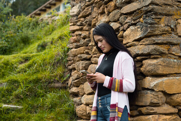 Joven atractiva con el pelo largo y negro parado cerca de una pared de roca con su celular en las manos, teléfono celular, naturaleza,